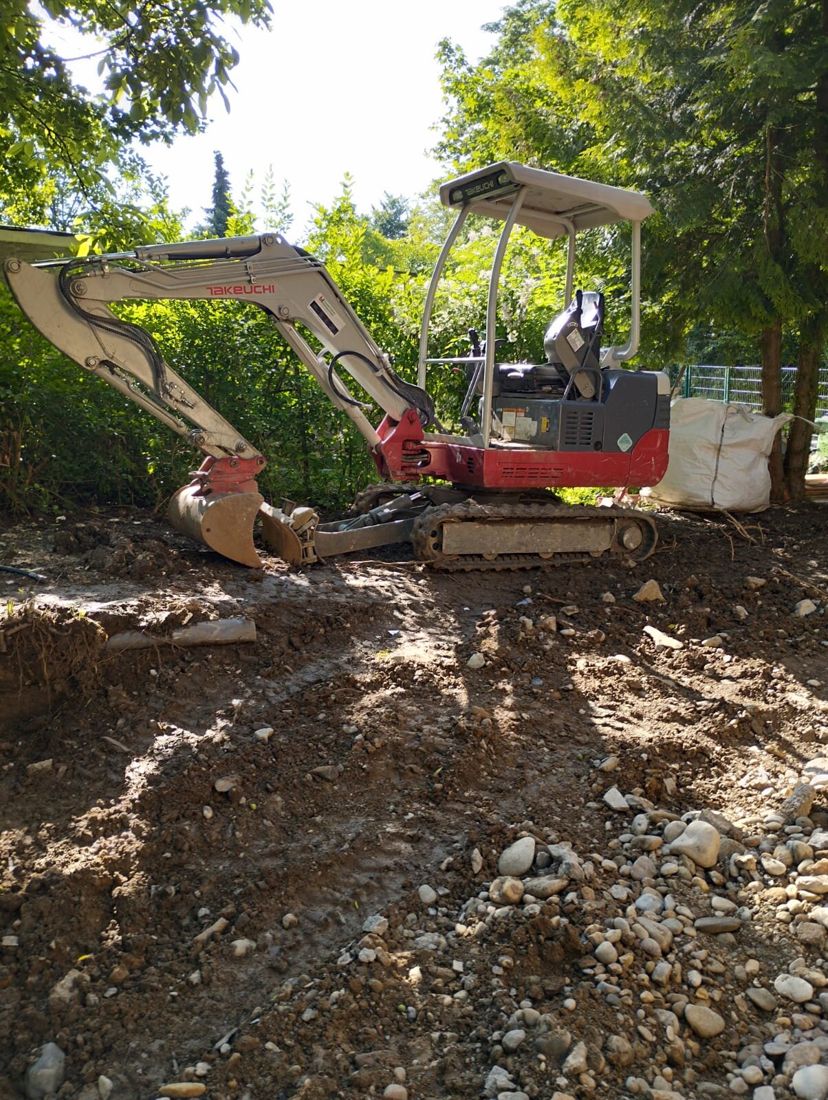 Bagger ebnet ein verwildertes Grundstück im Bezirk Mödling flächig ein und stellt ebenen Untergrund für Garten und Rasen her